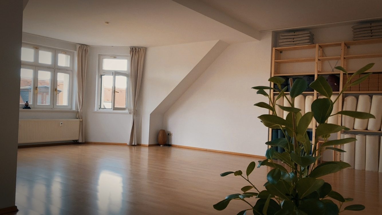 Workshopraum bei FREY in Leipzig: Großer Raum mit Dachschräge, hellem Holzboden, Fenstern und Regal mit Yogamatten