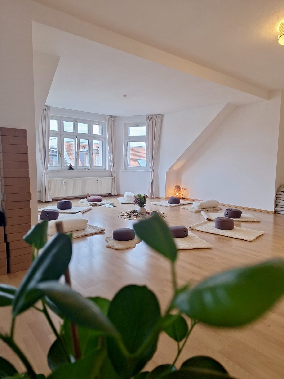 Seminarraum bei FREY mit Sitzkissen im Kreis, Kerzen und Blumen, helles Licht durch die Fenster