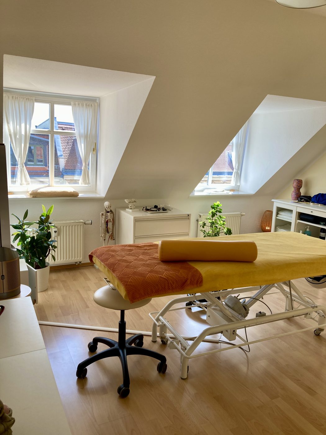Behandlungsraum bei FREY in Leipzig: Kleiner Raum mit Behandlungsliege unter der Dachschräge, Pflanzen und Tageslicht